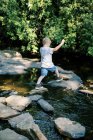 Un brave garçon de 5 ans sautant par-dessus des rochers dans une rivière — Photo de stock
