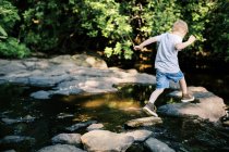 Um bravo de 5 anos saltando sobre rochas em um rio — Fotografia de Stock