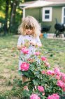 Petite fille debout près des roses dans son jardin — Photo de stock