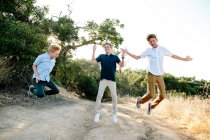 Trois garçons sautent dans les airs tout en souriant sur un sentier de randonnée — Photo de stock