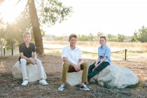 Retrato fuera de tres chicos sentados en grandes rocas - foto de stock