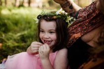 Junges Mädchen in Blumenkrone sitzt lächelnd auf Feld — Stockfoto
