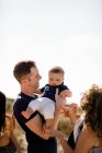 Papa tient bébé comme sourire de famille sur la plage — Photo de stock