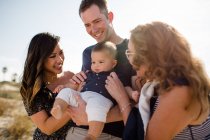 Родина посміхається, як тато тримає немовлятко на пляжі — стокове фото