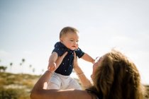 Nonnina holding nipote alto mentre standing su spiaggia — Foto stock