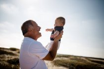 Дідусь тримає дідуся, стоячи на пляжі — стокове фото
