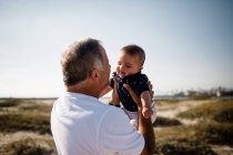 Grandfather Holding Grandson While Standing on Beach — Stock Photo