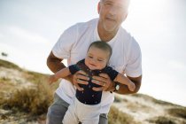 Großvater hält & spielt mit Enkel am Strand — Stockfoto