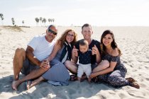 Famiglia di cinque seduti sulla spiaggia sorridente per la fotocamera — Foto stock