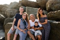 Famille de cinq personnes souriant pour une caméra assise sur des rochers à la plage — Photo de stock