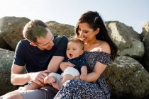 Eltern mit Mitte 30 halten Säugling am Strand auf Felsen — Stockfoto