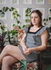 Elegante giovane donna si siede sulla sedia di fronte a piante e arte — Foto stock