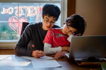 A father works from home at dining table with tween son on his lap — Stock Photo