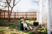 Молодий хлопчик обіймає коргі собаку, сидячи на подвір'ї теплиці — стокове фото