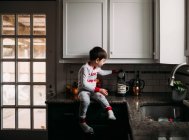 Young boy sitting on a counter and making coffee — Stock Photo