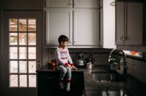 Jeune garçon assis sur un comptoir et faisant du café — Photo de stock
