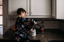 Jovem menino derramando leite na xícara de café — Fotografia de Stock