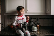 Preschool age boy sitting on a kitchen counter with milk on his face — Stock Photo