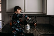 Мальчик наливает молоко в кофейную чашку — стоковое фото