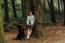 Femme avec deux chiens dans la forêt appuyé contre un arbre moussue — Photo de stock