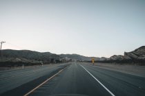Пустое шоссе в Калифорнии Сразу после заката с желтой дорожной надписью и горами вдалеке во время пандемии коронавируса — стоковое фото