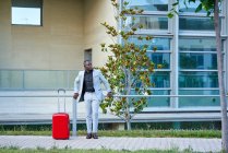 African-American in a white suit and a red suitcase. Businessman. Businessman traveling on business. Traveling man. — Stock Photo