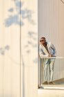 Un homme d'affaires afro-américain au coucher du soleil dans un immeuble. Il se prélasse au soleil du soir. L'ombre d'un arbre est projetée sur le mur — Photo de stock