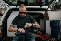 Homem sentado na parte de trás do caminhão preparando cordas de escalada — Fotografia de Stock