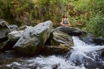 Mujer joven practicando yoga en un río. Está en medio de la naturaleza.. - foto de stock