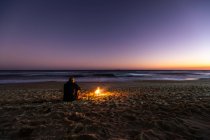 Вид ззаду самотнього хлопця і багаття на пляжі на заході сонця — стокове фото