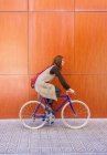 Красива молода жінка в окулярах їде на велосипеді проти червоної стіни . — стокове фото