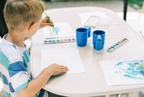 Маленький хлопчик малює акварелями зовні на патіо — стокове фото