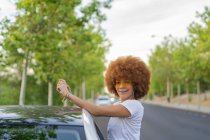 Mulher com cabelo afro tirar uma foto com seu smartphone ao lado de seu carro branco — Fotografia de Stock