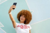 Mujer con cabello afro tomando una selfie con su smartphone - foto de stock