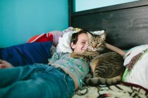 Boy smiles with half of his face blocked by his cat snuggling him — Stock Photo