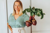 Young woman holding beetroots with green leaves and smiling — Stock Photo
