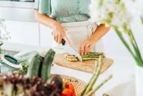 Donna che taglia asparagi su un tagliere a tavola — Foto stock