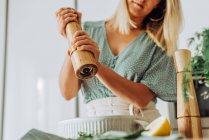 Mujer europea joven moliendo pimienta en bandeja con codorniz para asar - foto de stock