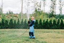 Boy standing with a hose spraying water at home in the yard — Stock Photo
