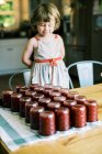 Kleines Mädchen blickt auf die Gläser mit frisch gekochter Pflaumenmus-Marmelade — Stockfoto