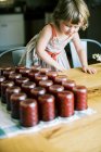 Petite fille regardant les pots de pflaumenmus frais cuit — Photo de stock