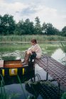 Donna seduta su un molo di legno vicino alla barca — Foto stock