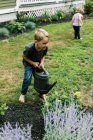 Хлопчик допомагає з поливом рослин в саду — стокове фото