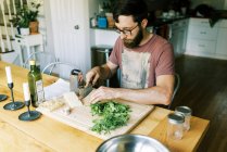 Un giovane uomo che taglia basilico fresco fatto in casa per il pesto fatto in casa — Foto stock
