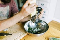 A young man grating parmesan cheese for homemade pesto — Stock Photo