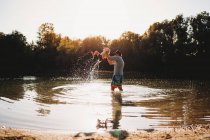 Padre sosteniendo a un niño pequeño en el aire en el lago salpicando agua - foto de stock