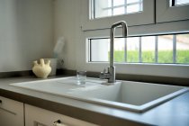 Современный кухонный интерьер с белой раковиной и большим окном — стоковое фото