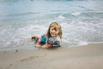 Молодая девушка лежит в воде на пляже улыбаясь — стоковое фото
