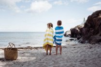 Хлопчик і дівчина стояли на пляжі, загорнуті в рушники, дивлячись на океан — стокове фото