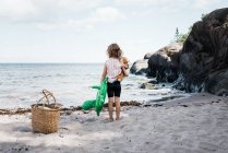 A menina estêve na praia que prende seu urso e inflável pelo mar — Fotografia de Stock